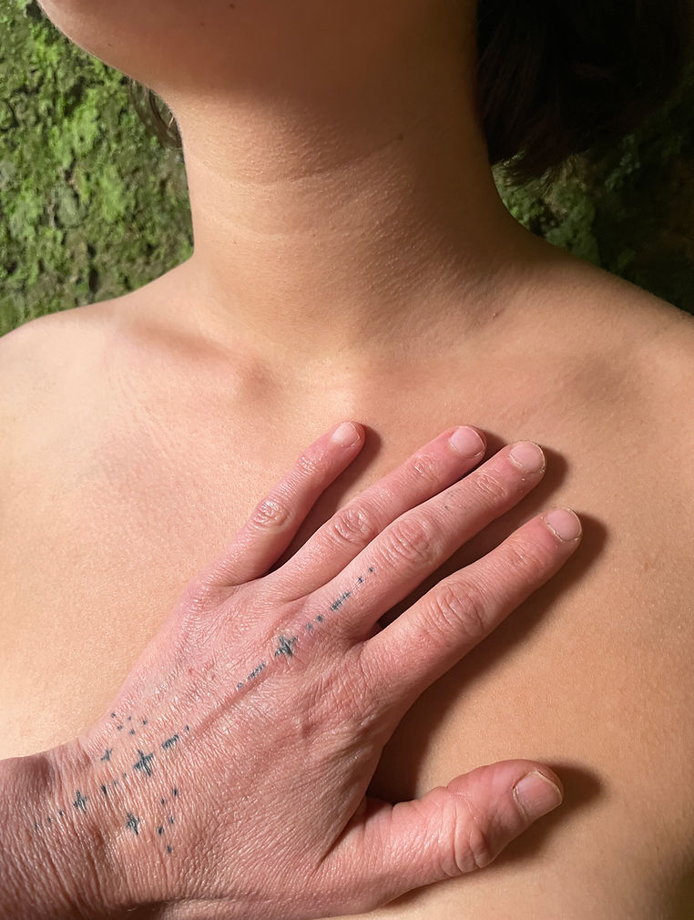 Eine Hand liegt ruhig auf der Brust, im Hintergrund bemooste Rinde